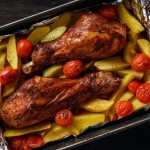 baked turkey legs with potatoes and tomatoes in a baking dish with foil
